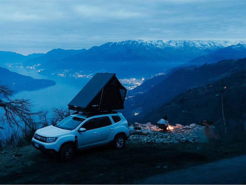 Cargo 2.0 rooftop tent on a white SUV set against snow-capped mountains at sunset, with a campfire nearby.