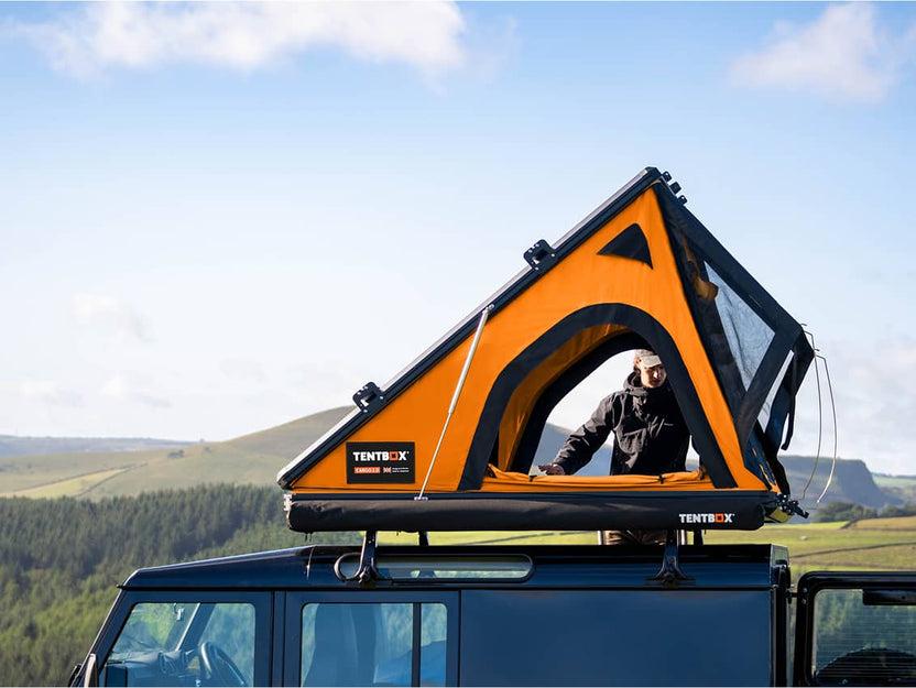 A man peeking out from an orange-accented Cargo 2.0 rooftop tent on top of a 4x4