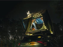 Nighttime scene of a car with the Cargo 2.0 glowing from inside under string lights, ladder extended.