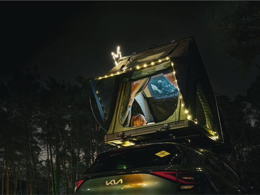 Nighttime scene of a car with the Cargo 2.0 glowing from inside under string lights, ladder extended.