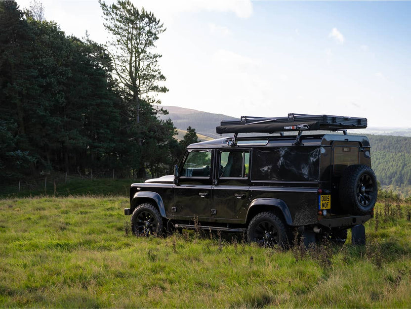 Cargo 2.0 set up on a black Land Rover Defender, parked on grass with tent deployed and awning visible.