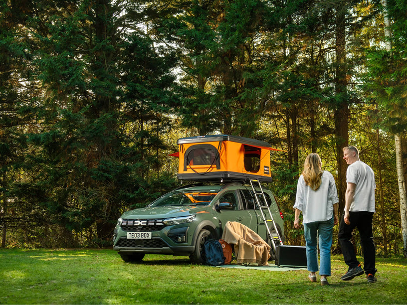 Two people standing next to a car with a TentBox Classic rooftop tent in Sunset in a forest setting.