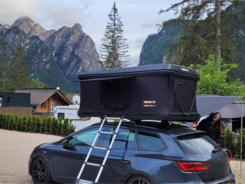 Family unpacking the TentBox Classic in a scenic alpine setting, car parked near wooden cabins