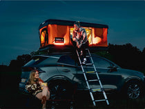 TentBox Classic glowing at night with a couple enjoying a drink by the car