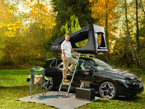 Man setting up a TentBox GO rooftop tent on a car in a forest during autumn.