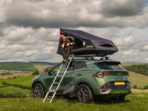 Person using a TentBox GO rooftop tent on a green SUV with a scenic background