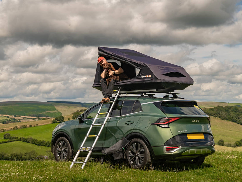 Person using a TentBox GO rooftop tent on a green SUV with a scenic background