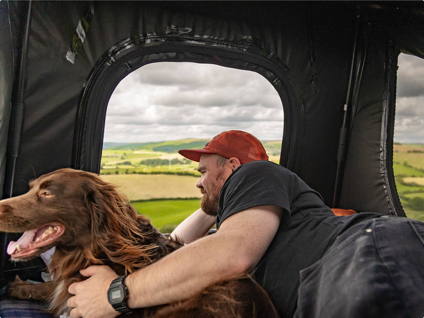 Man and his dog peering out from inside the GO tent with the door unzipped; joyful and cozy vibe.

