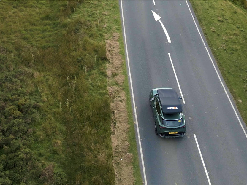 Aerial road shot of a car driving with the GO tent mounted on top, illustrating slim profile during transit.

