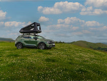 GO tent opened on a parked vehicle in a field full of wildflowers and mountains in the background.

