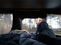 Man lounging inside the GO tent with mesh windows on either side, soaking in the forest view.

