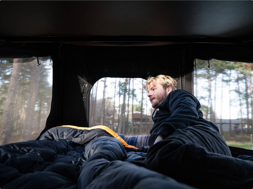 Man lounging inside the GO tent with mesh windows on either side, soaking in the forest view.


