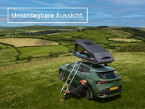 GO Dachzelt vollständig aufgebaut auf einem Auto auf einem Hügel-Campingplatz, mit ausgefahrener Leiter; im Hintergrund eine üppige Landschaft.