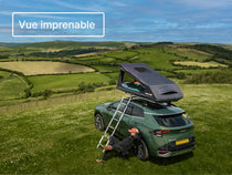 Tente GO entièrement déployée sur une voiture, dans un camping au sommet d’une colline, avec l’échelle dépliée et une campagne verdoyante en arrière-plan.

