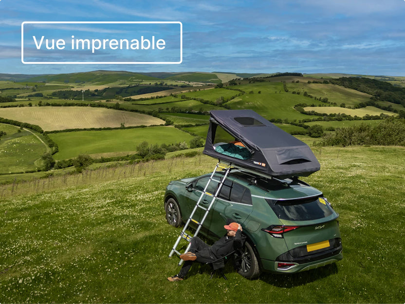 Tente GO entièrement déployée sur une voiture, dans un camping au sommet d’une colline, avec l’échelle dépliée et une campagne verdoyante en arrière-plan.

