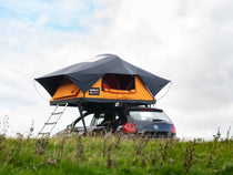 TentBox Lite 2.0 in the Sunset Orange colour, parked in a field on top of a mountain.