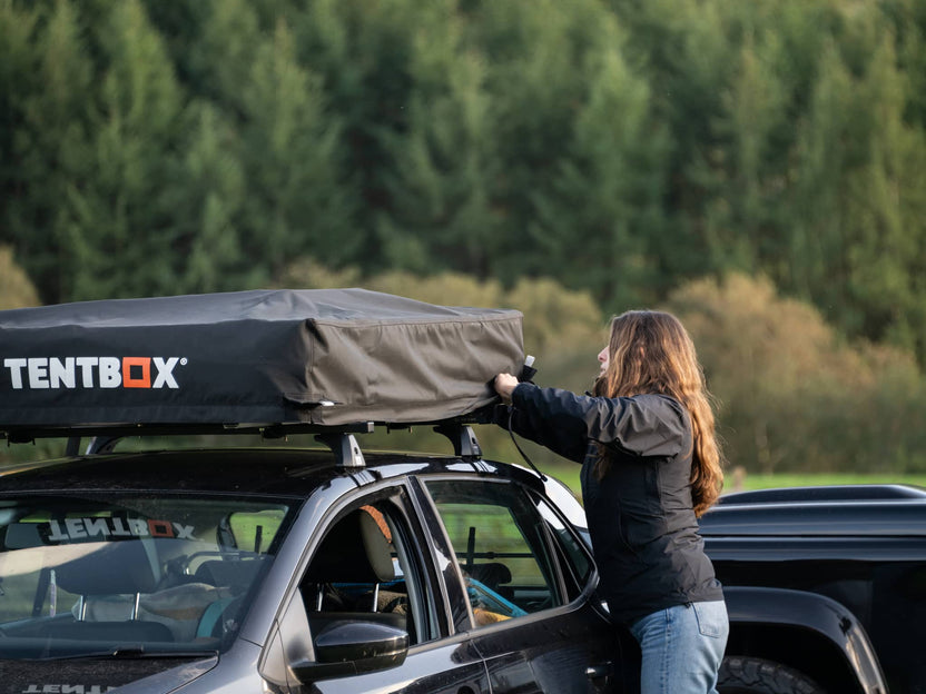 Opening the TentBox Lite 2.0 in a campsite, set against a backdrop of pine trees.