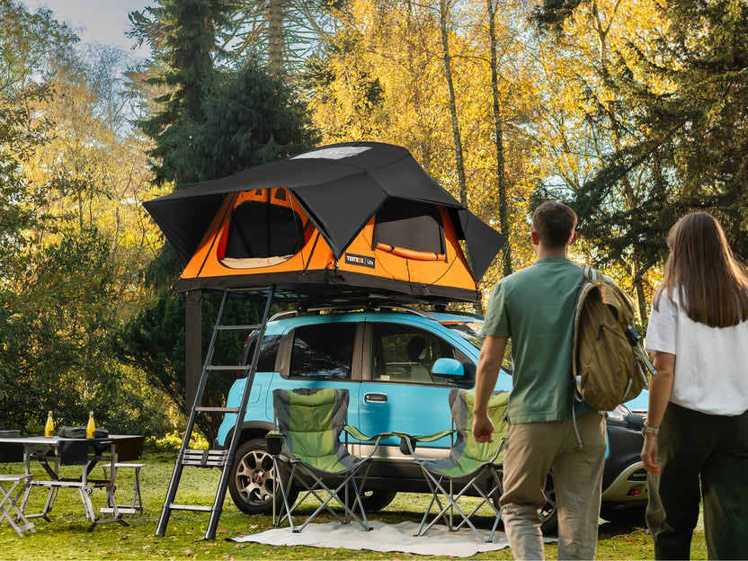 Two people walking towards a blue car with a TentBox Lite roof tent in a forest setting.