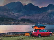 Scenic view of a car with a TentBox Lite 2.0 parked by a lake, with a mountain range in the background