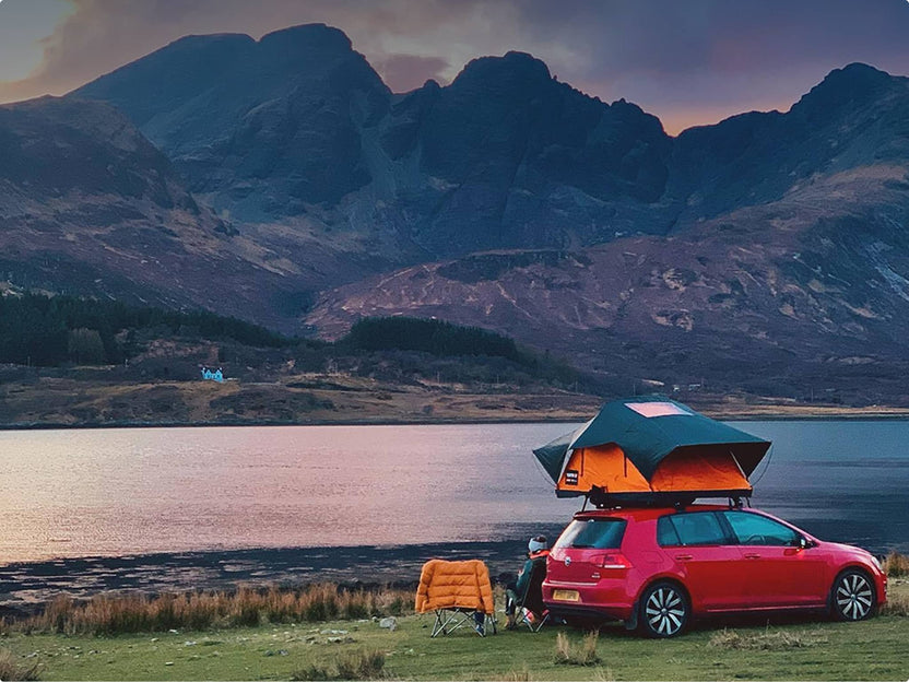 Scenic view of a car with a TentBox Lite 2.0 parked by a lake, with a mountain range in the background