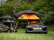 TentBox Lite XL in the Sunset Orange colour, parked in a field near the TentBox Lite 2.0.