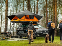 TentBox Lite XL roof tent on a car in a forest with people and a dog heading back to camp
