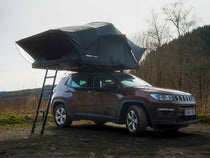 A brown SUV with a TentBox Lite XL roof tent on top, opened in a natural campsite forest setting