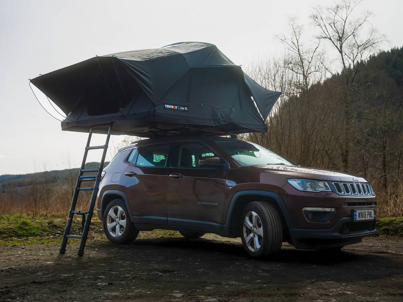 A brown SUV with a TentBox Lite XL roof tent on top, opened in a natural campsite forest setting