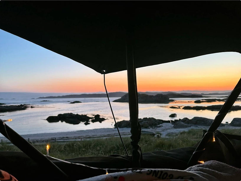 Sunset view through the mesh windows of a TentBox set up by a lake, with pink and golden light
