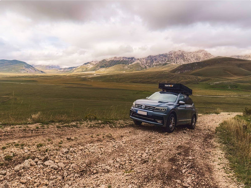 A black SUV driving across a rugged hilltop landscape with a TentBox installed